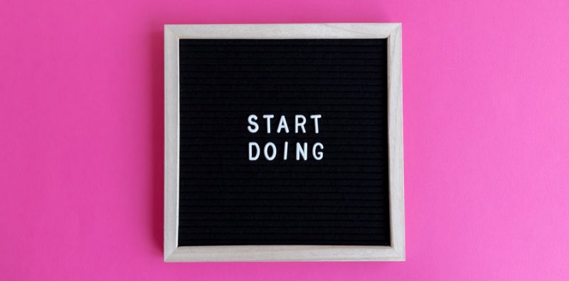 Black letter board with 'Start Doing' motivational text on bright pink background.