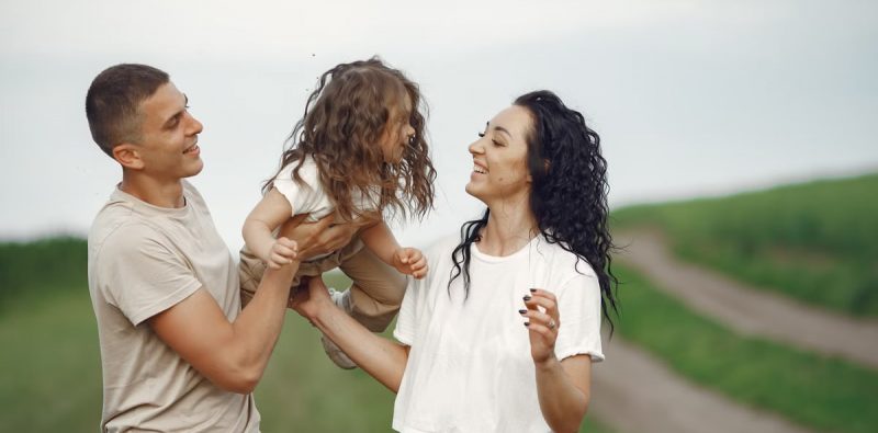 A joyful family moment outdoors with parents playing with their daughter.